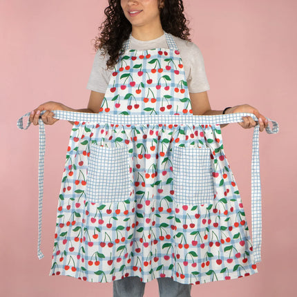 Person wearing a colorful apron with cherry pattern on a pink background